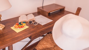 Un escritorio de madera con un libro abierto, un plato de fruta, gafas de sol y un sombrero blanco.