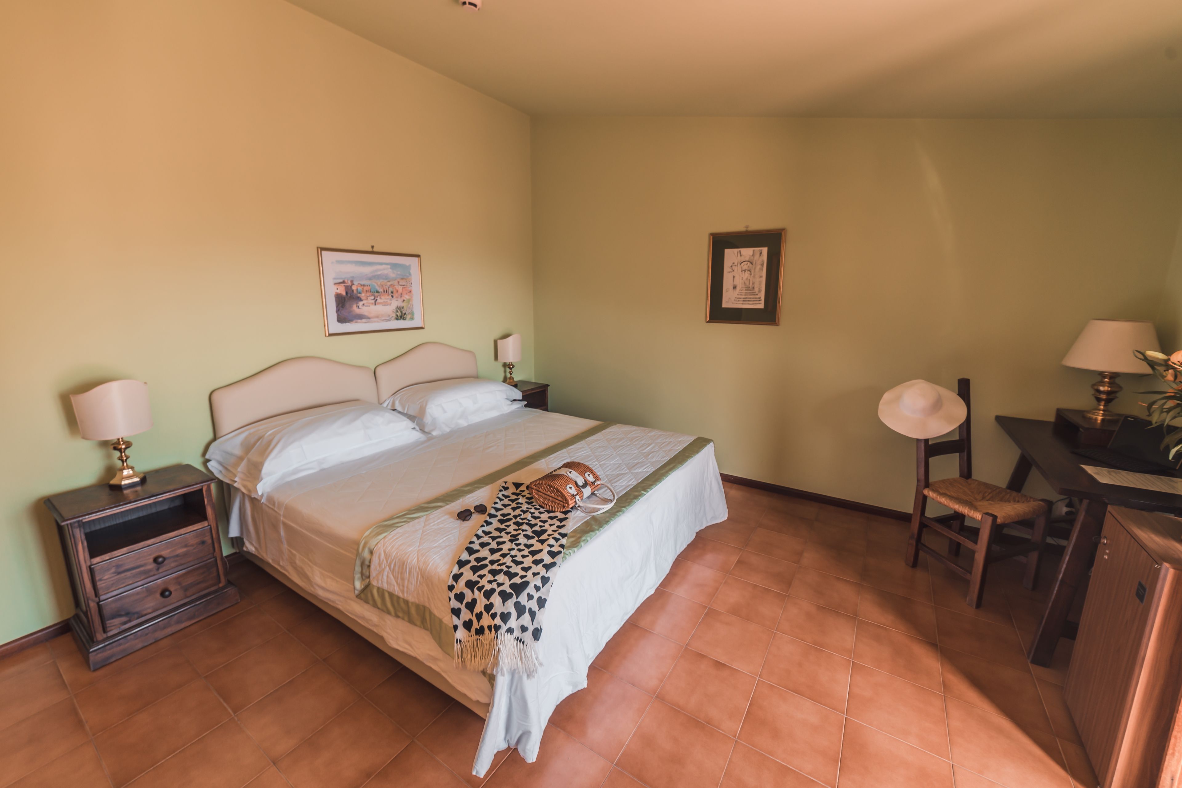 A neatly arranged bedroom with a bed, bedside tables, a desk, and chairs.