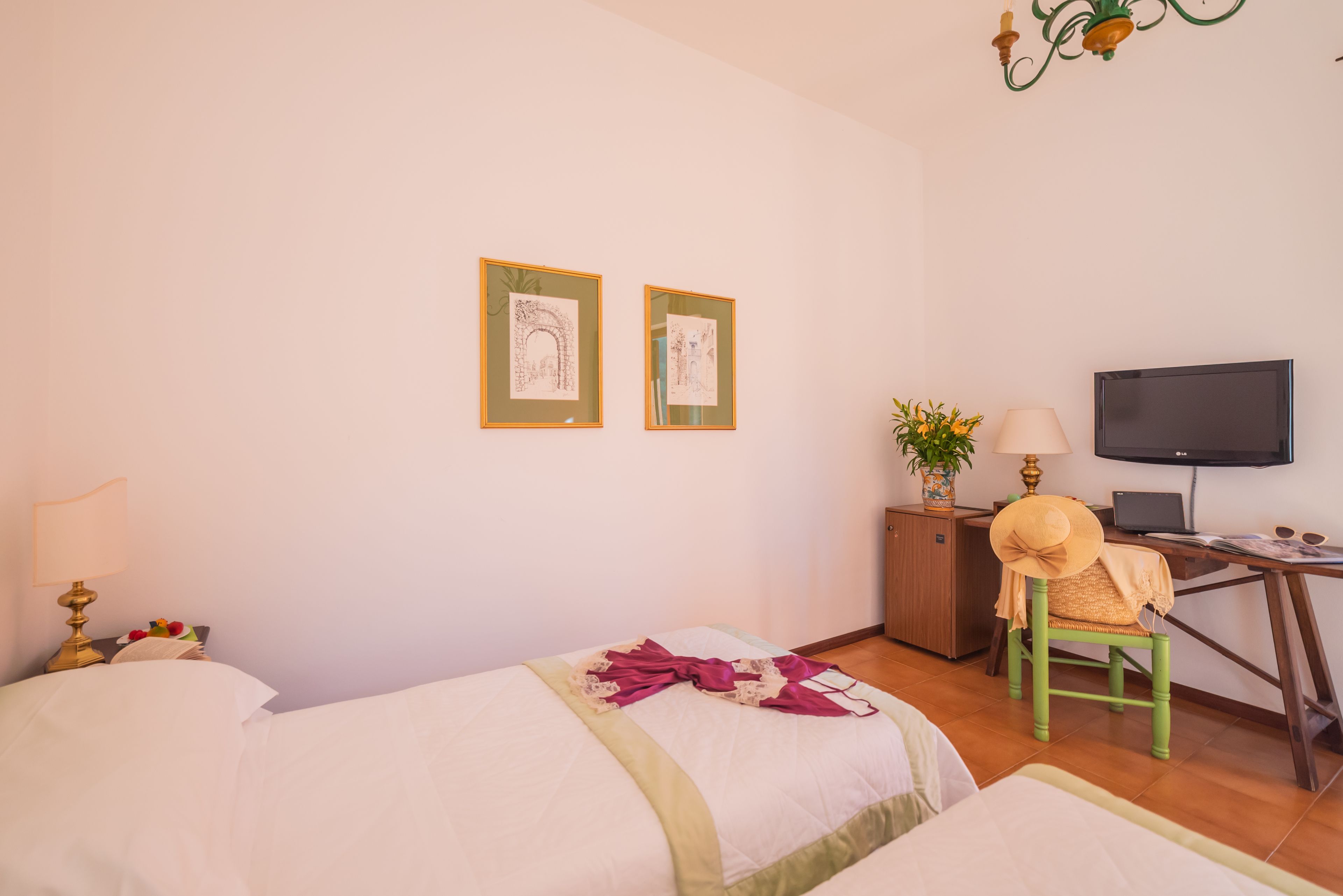 Une chambre d’hôtel avec deux lits, un bureau avec un ordinateur, une télévision et deux œuvres d’art encadrées accrochées au mur.