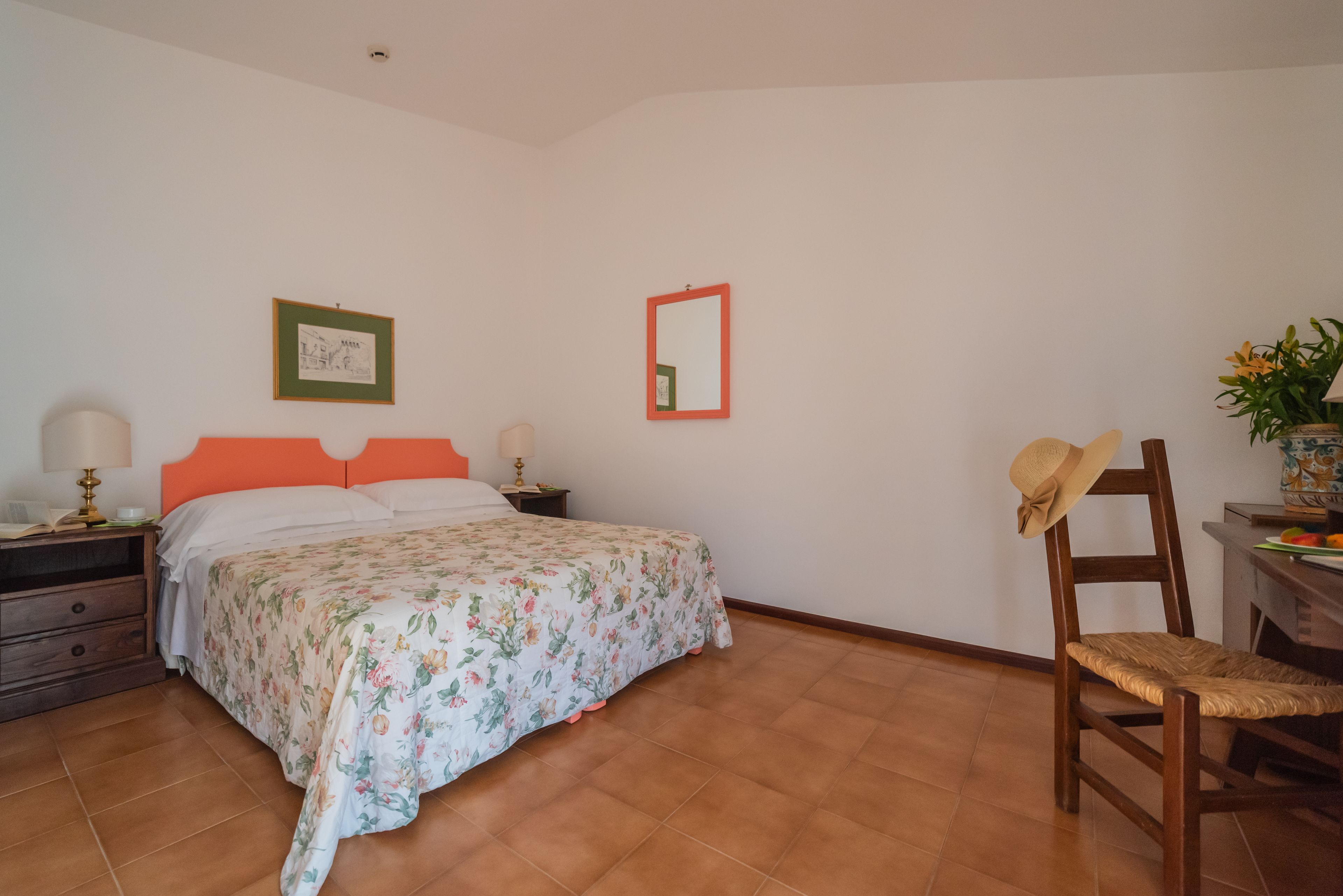 A bedroom with a bed, a nightstand, a chair, a mirror, and a framed picture on the wall.
