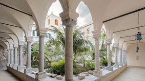 Stroll through this serene, classical courtyard, surrounded by arches and columns, amidst lush greenery and a Mediterranean-inspired backdrop.