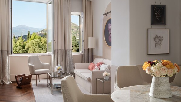 A modern living room with a sofa, armchairs, a coffee table, and a dining table. There is a view of a mountainous landscape through large windows. - San Domenico Palace, Taormina, A Four Seasons Hotel (Taormina)