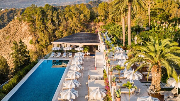 A rooftop pool area with lounge chairs and umbrellas, surrounded by lush greenery and a mountain in the background. - San Domenico Palace, Taormina, A Four Seasons Hotel (Taormina)