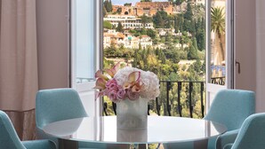 A balcony with a table and chairs, a vase with flowers, and a view of a historic town. - San Domenico Palace, Taormina, A Four Seasons Hotel (Taormina)