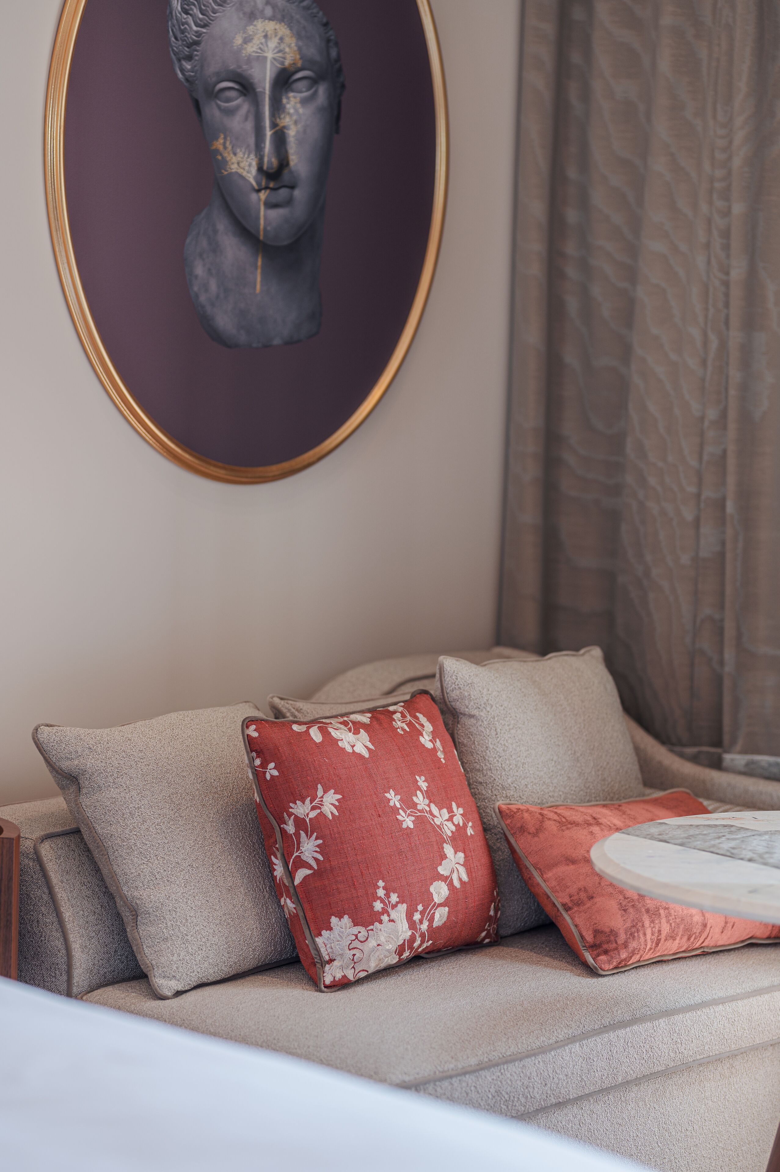 A sofa with multiple cushions, a framed artwork above, and a patterned curtain in the background.