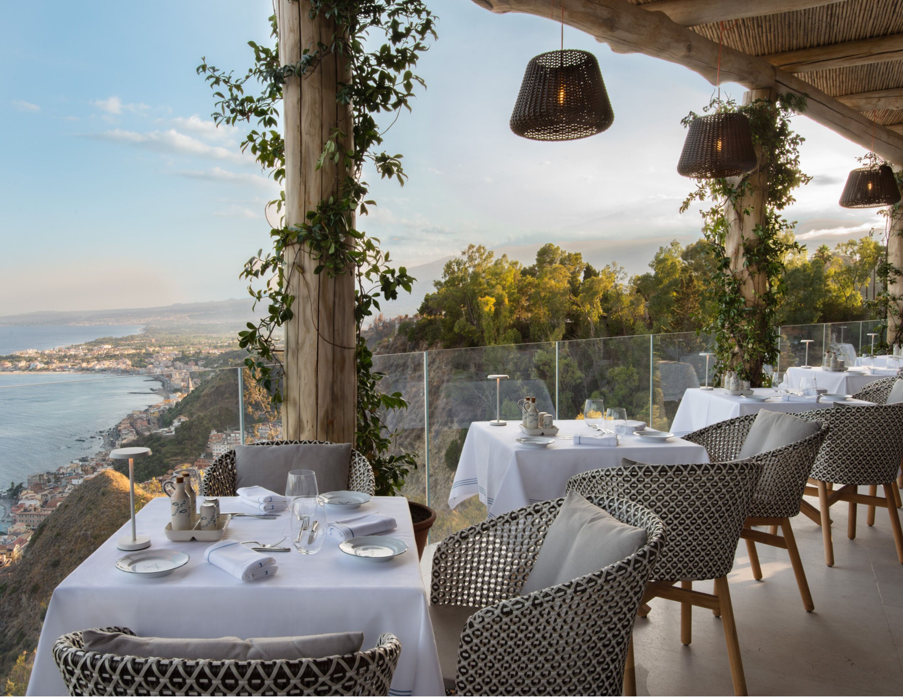 Un espace extérieur aménagé pour les repas, avec des tables pour deux personnes, offrant une vue sur un paysage côtier.