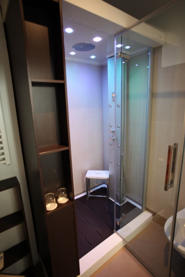 A modern bathroom with a glass shower enclosure, a built-in bench, and a shelf with two glasses.