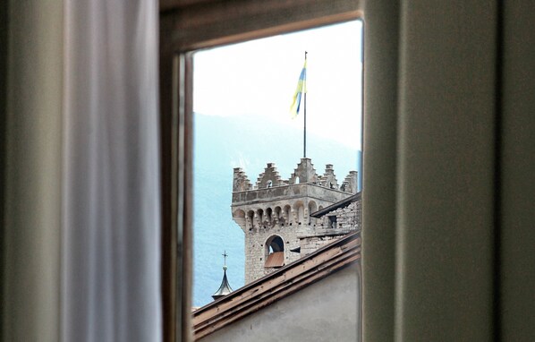 A view of a historic tower with a flag, through a window with curtains.