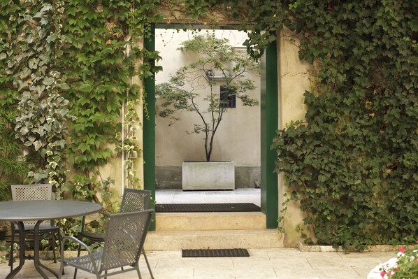 A patio area with a round table and two chairs, a potted plant, and a concrete planter.