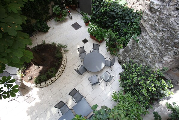 An outdoor patio with round tables and chairs, surrounded by potted plants and a stone wall.