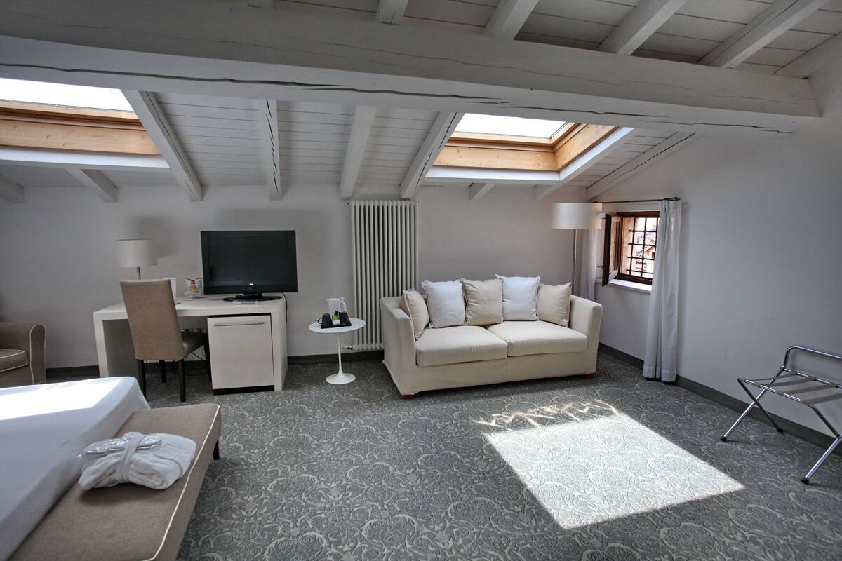Une chambre d’hôtel comprenant un lit, un canapé, un bureau avec une télévision, une petite table avec une lampe et un radiateur.