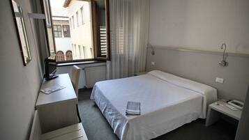 Ein Hotelzimmer mit Bett, Schreibtisch, Stuhl, einem Fenster mit Vorhängen und Blick auf Gebäude.