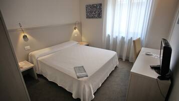 Ein Hotelzimmer mit Bett, Nachttischen, einem Schreibtisch mit Computer und einem Fenster mit Vorhängen.
