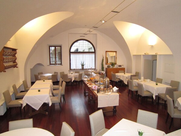 A dining area with tables and chairs, arched ceiling, and a large window.