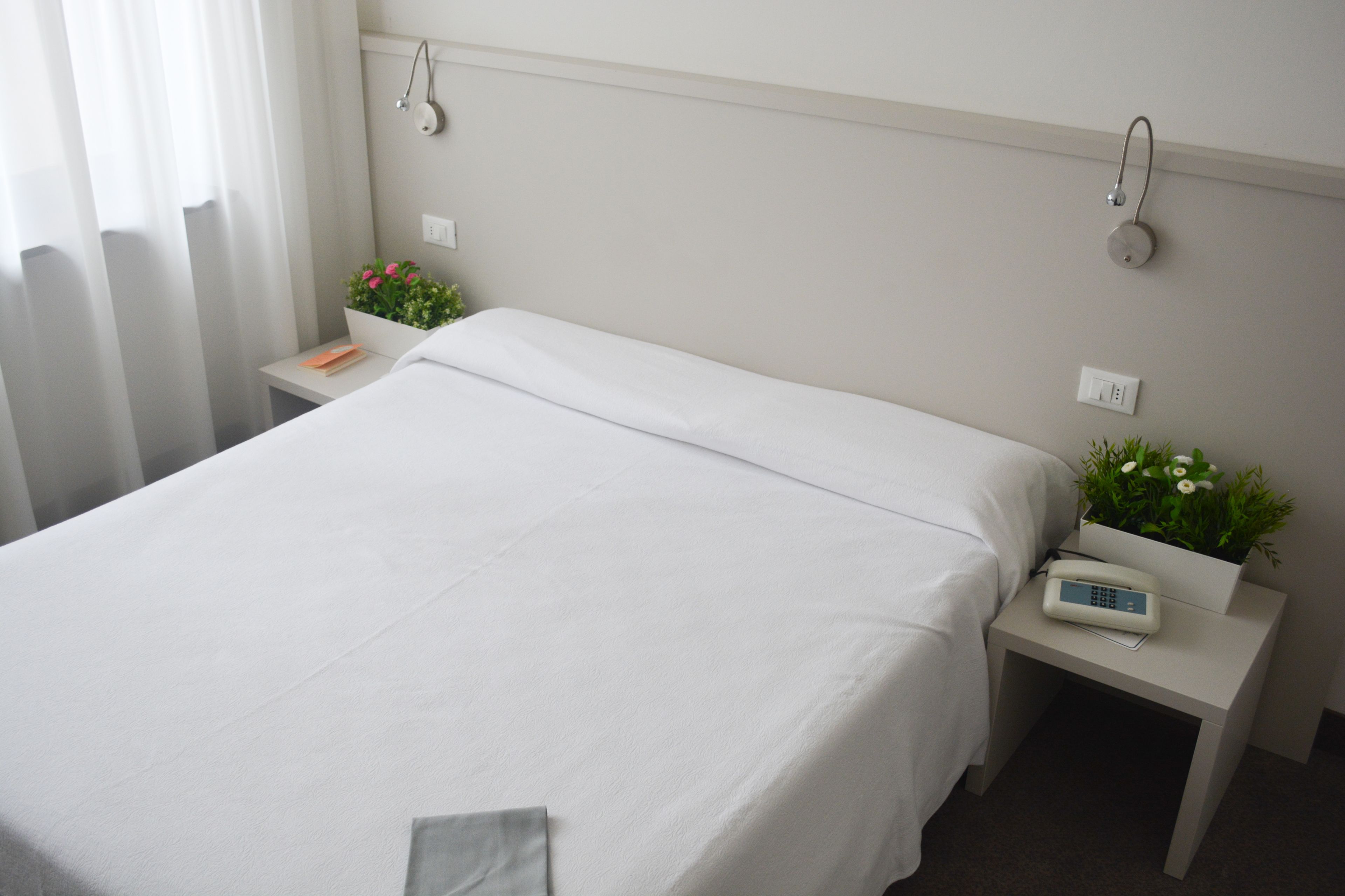 Un letto rifatto con cura in una camera d'albergo, con un comodino, una piccola pianta in vaso e una lampada da tavolo.