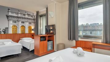 Een hotelkamer met een groot bed, twee kleinere bedden, een houten kast met een magnetron, een televisie en een raam met gordijnen.