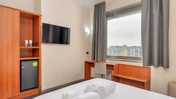 Habitación de hotel con cama, escritorio, televisor, minibar y ventana con cortinas.
