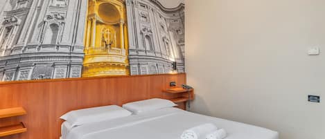 A hotel room with a bed, a wooden headboard, a wall-mounted phone, and a wall-mounted thermostat.