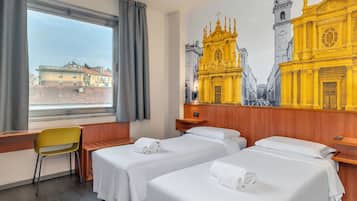 A hotel room with two beds, a wooden desk, a chair, and a large window.