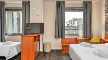 Een hotelkamer met twee bedden, een bureau, een televisie en uitzicht op gebouwen.