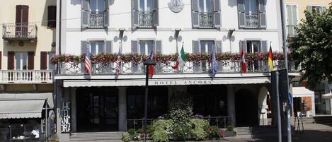 A hotel with a white facade, multiple balconies with flower boxes, and flags.