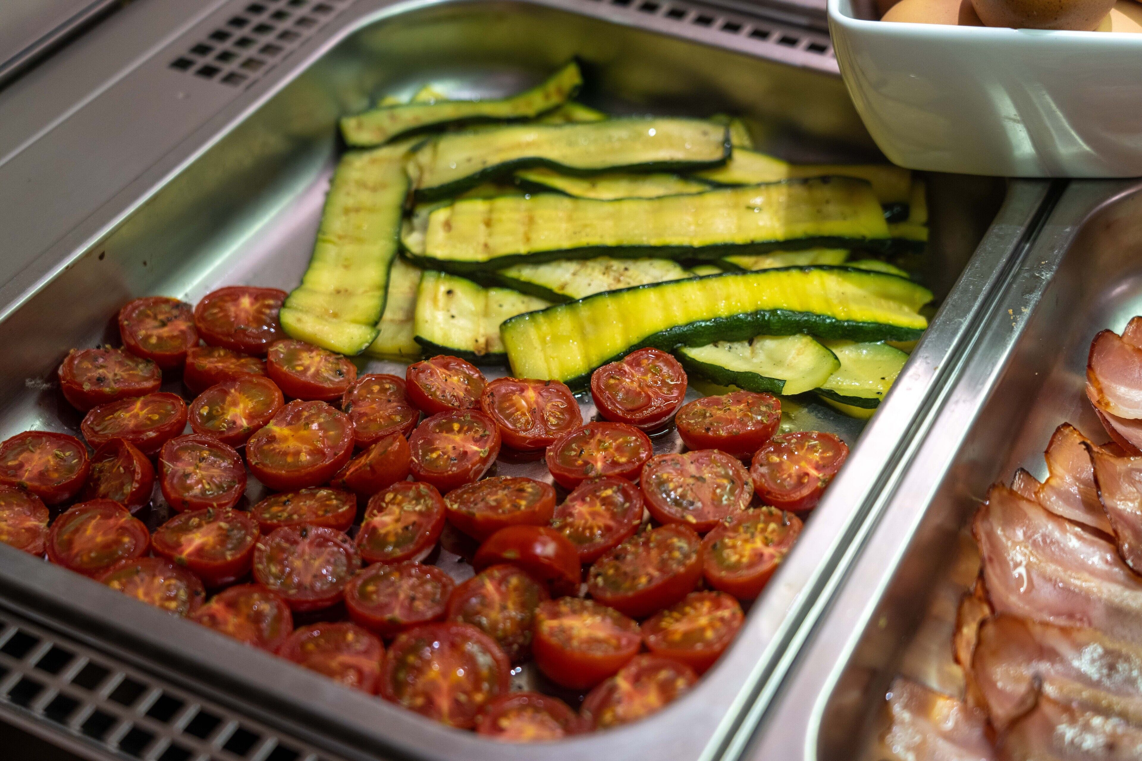 A buffet with sliced cucumbers, cherry tomatoes, and sliced ham.