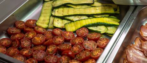 A buffet with sliced cucumbers, cherry tomatoes, and sliced ham.