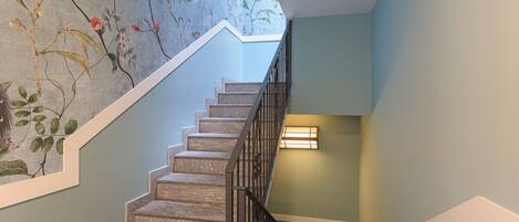 A staircase with a floral mural on the wall, a light fixture on the landing, and a metal railing.
