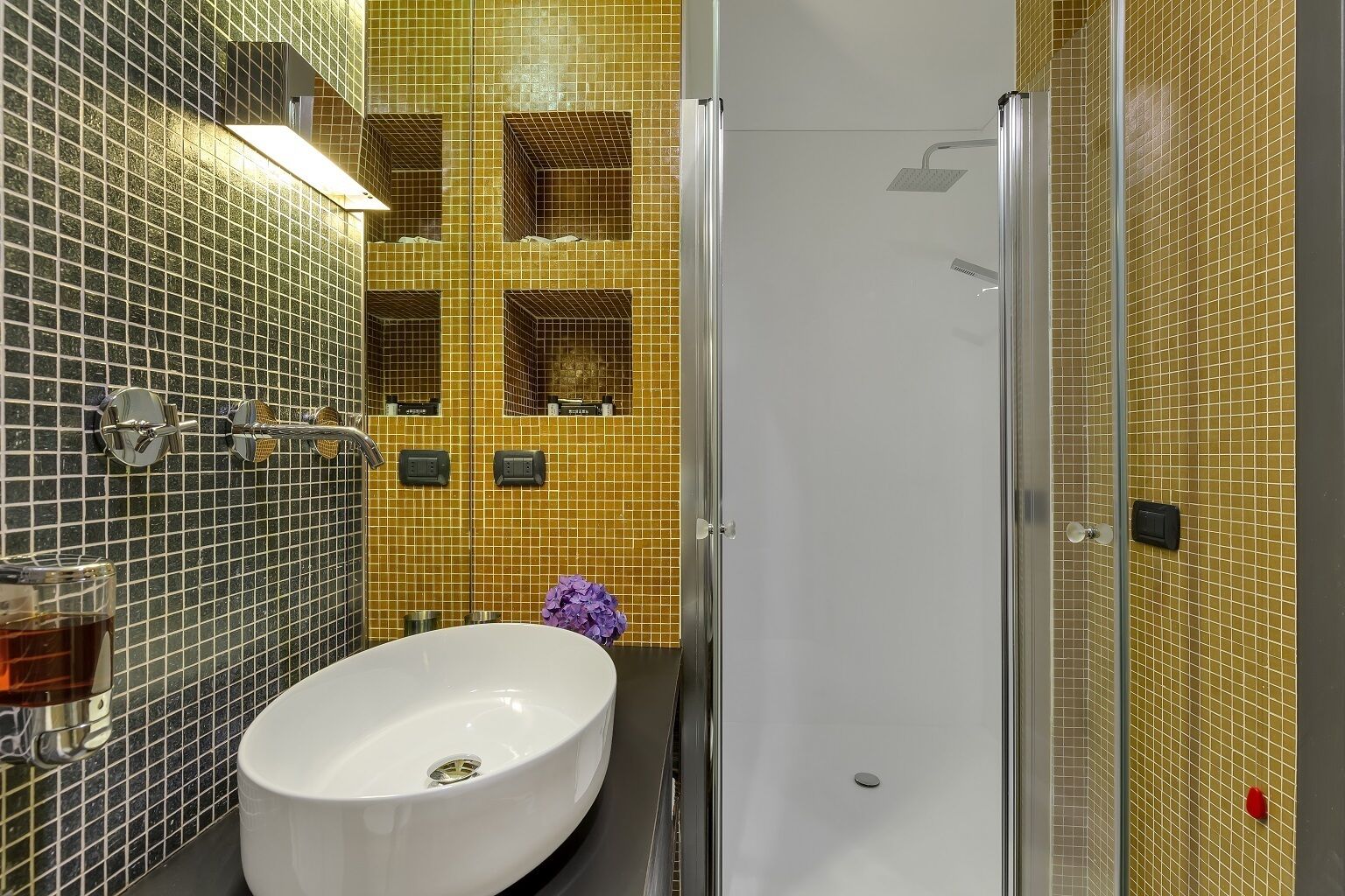 Un baño con un lavabo blanco, cabina de ducha con paredes de vidrio y pared revestida con azulejos amarillos.
