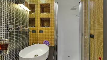Un baño con un lavabo blanco, cabina de ducha con paredes de vidrio y pared revestida con azulejos amarillos.