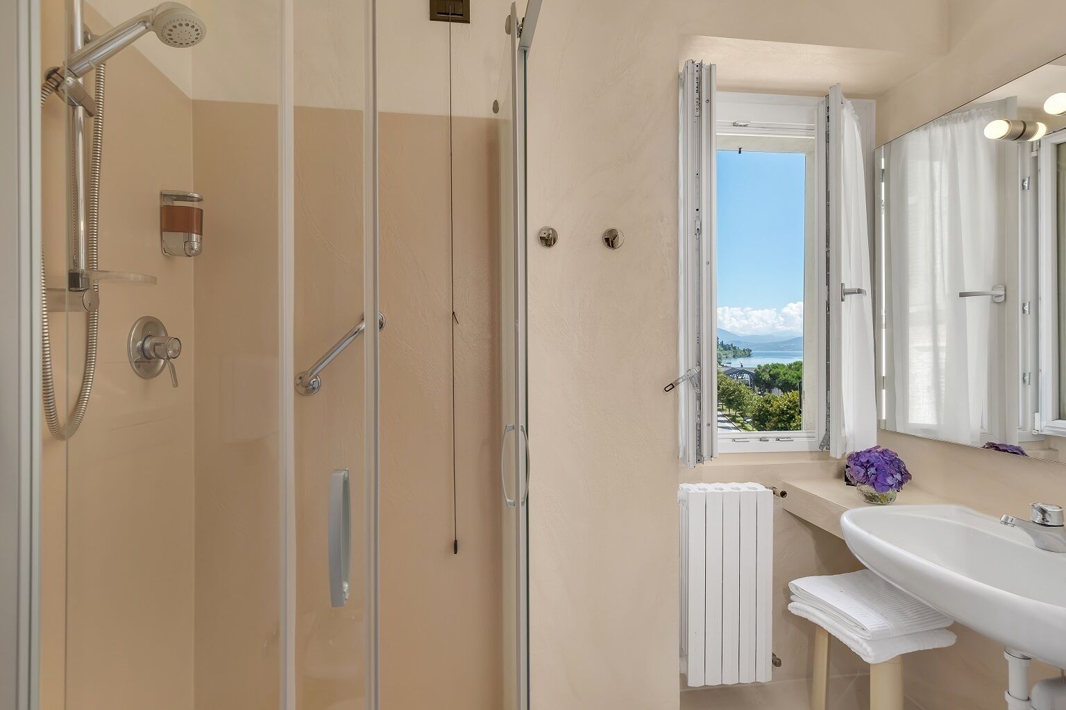 Ein Badezimmer mit Duschkabine aus Glas, einem weißen Waschbecken und einem Fenster mit Blick ins Freie.