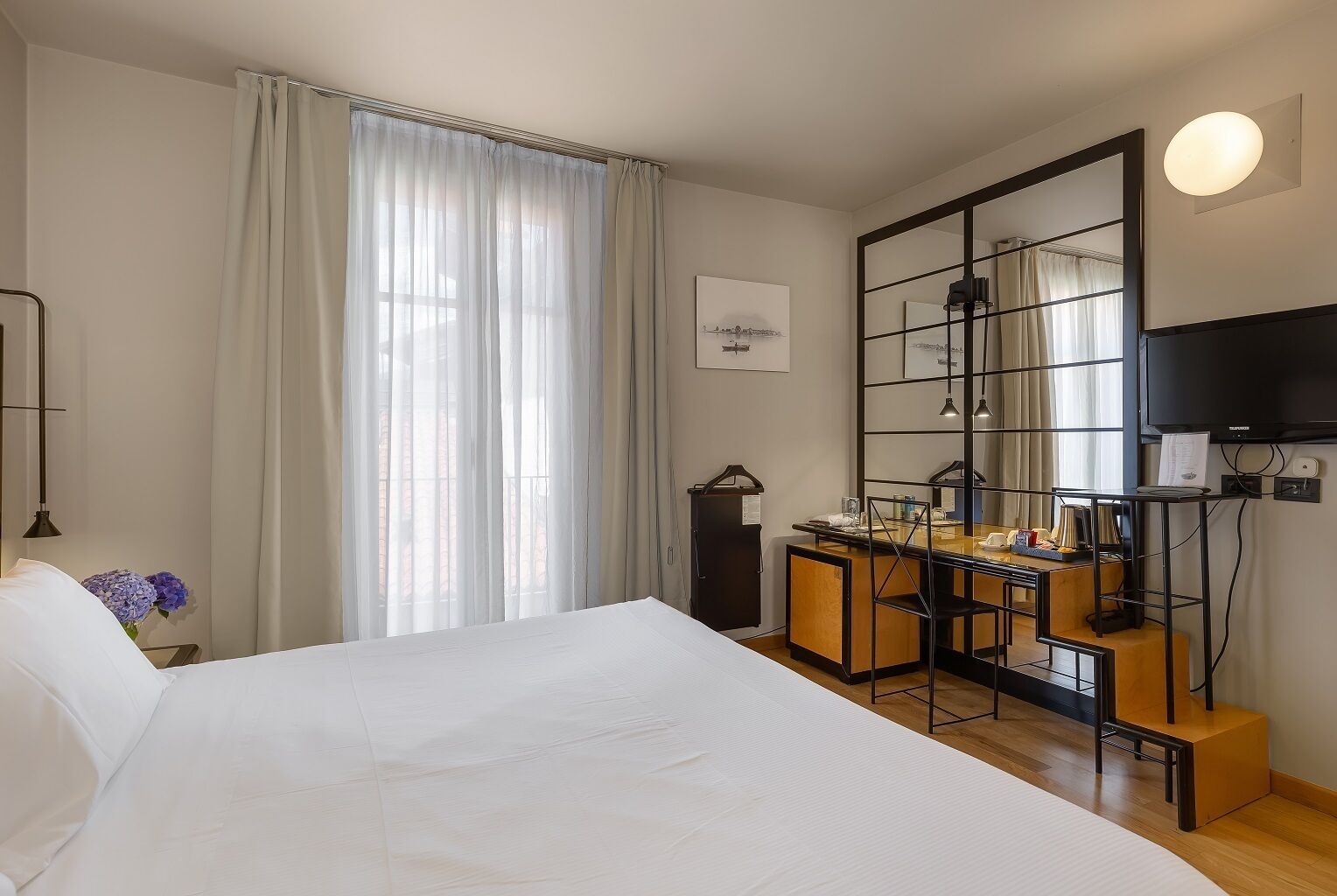 A hotel room with a large bed, a desk with a chair, a television, and a mirror.