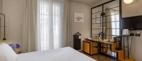 A hotel room with a large bed, a desk with a chair, a television, and a mirror.