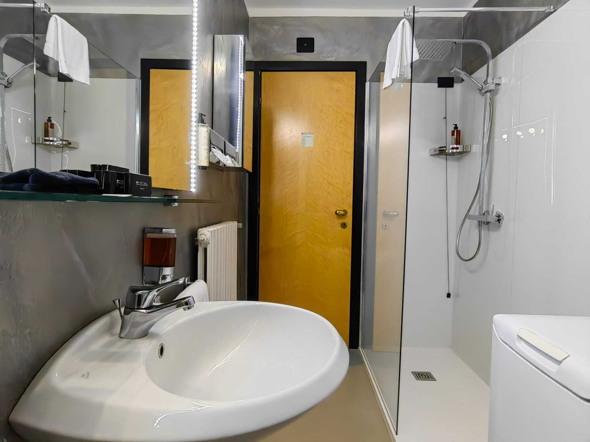 A modern bathroom with a large white sink, a mirror, a shower, and a toilet.