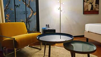 A modern living room with a yellow armchair, a glass-top coffee table, and a sofa. There is a painting on the wall and a floor lamp.