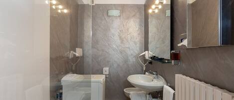 Un baño moderno con cabina de ducha de vidrio, un lavabo blanco y un espejo grande.