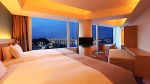 Habitación de hotel con una cama grande, televisión, escritorio y vista a un paisaje urbano de noche.
