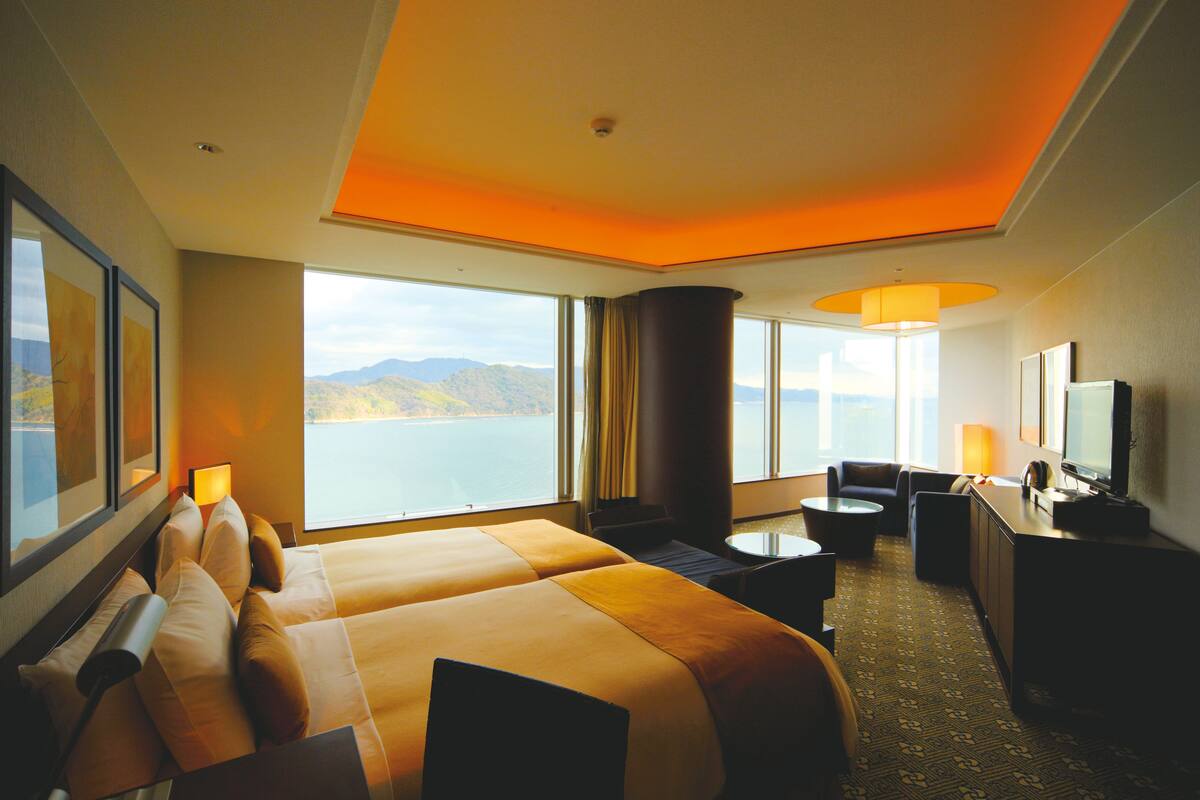 A hotel room with a large bed, a desk, a chair, a TV, and a view of the sea.