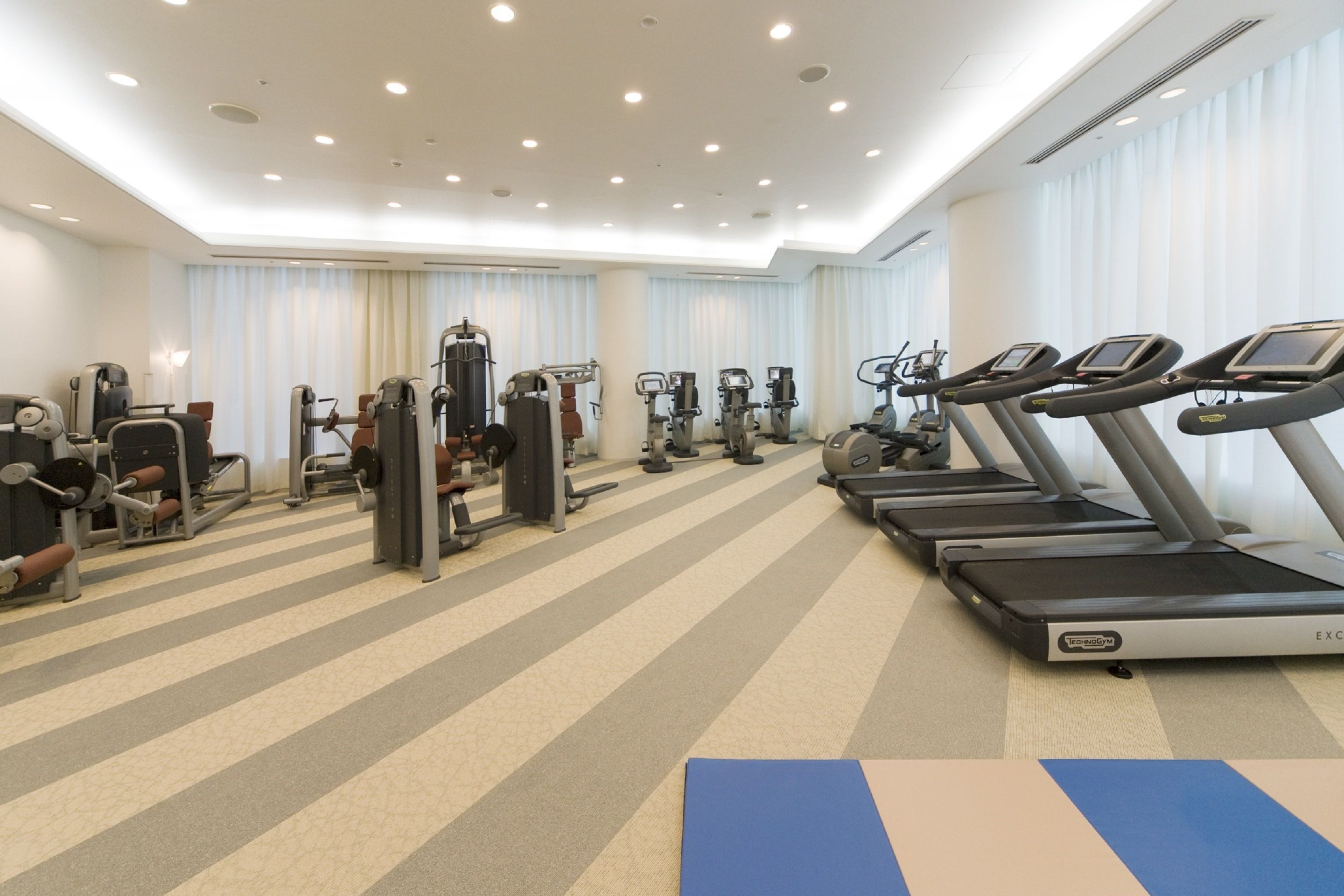 Un gimnasio con cintas de correr, máquinas de pesas y colchonetas de ejercicio.