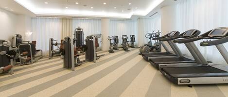 Un gimnasio con cintas de correr, máquinas de pesas y colchonetas de ejercicio.