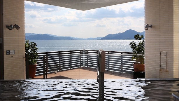 Zona de spa con vista a un lago y montañas, con terraza de madera y paredes de azulejos.