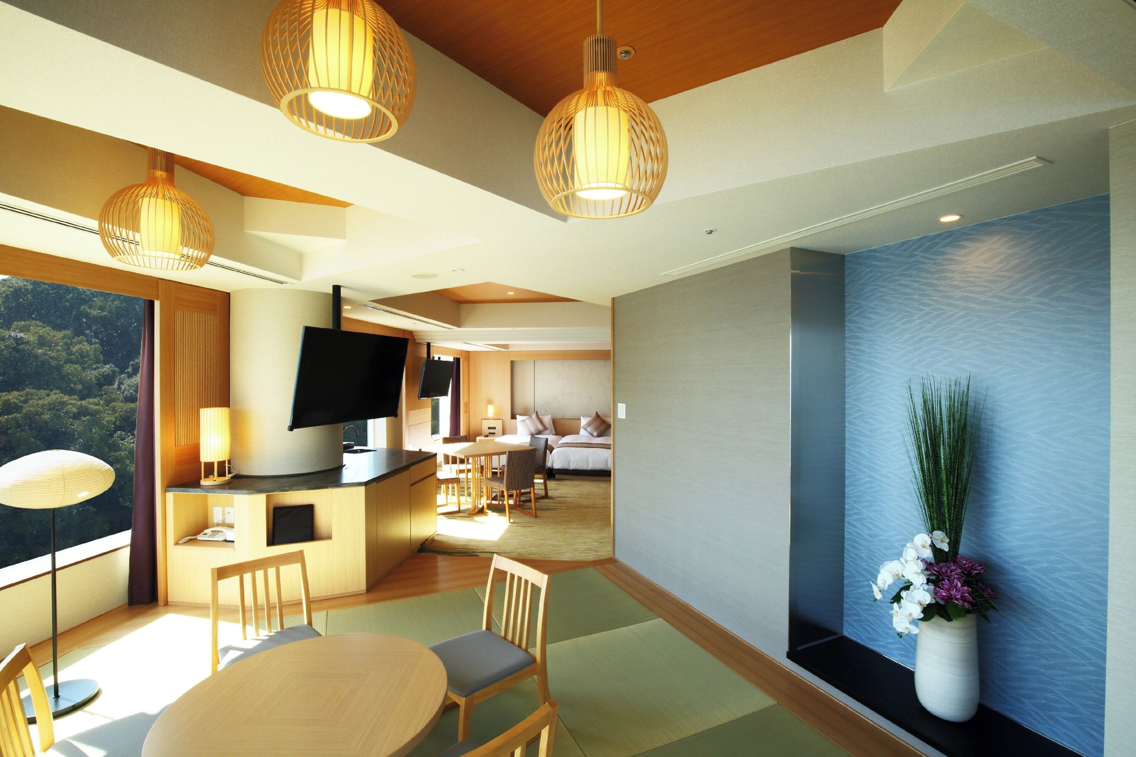 A modern hotel room with a dining area, a TV, and a large window offering a view of the outdoors.