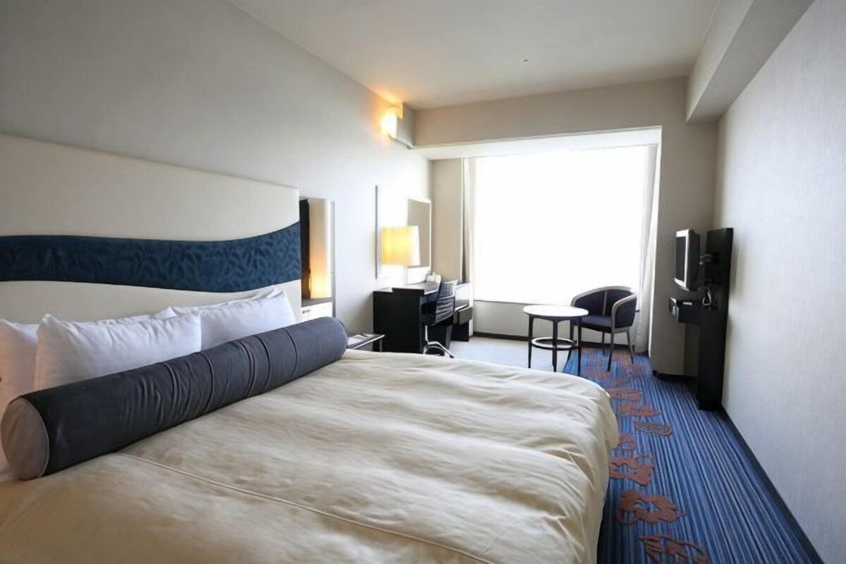 Una habitación de hotel con una cama grande, un escritorio, una silla, un televisor y una ventana.
