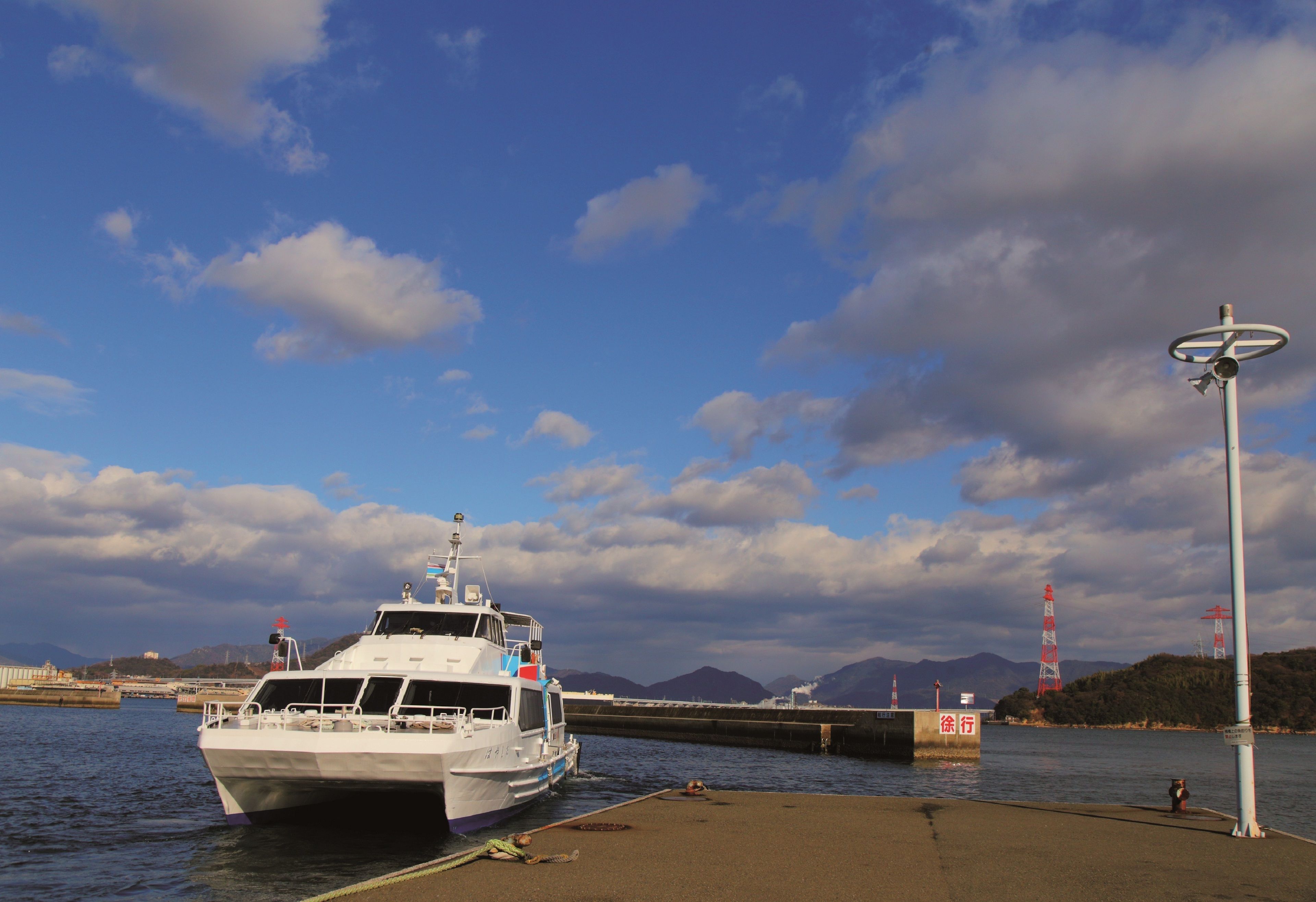 Een veerboot aanmeren bij een steiger, met een heldere lucht en bergen op de achtergrond.