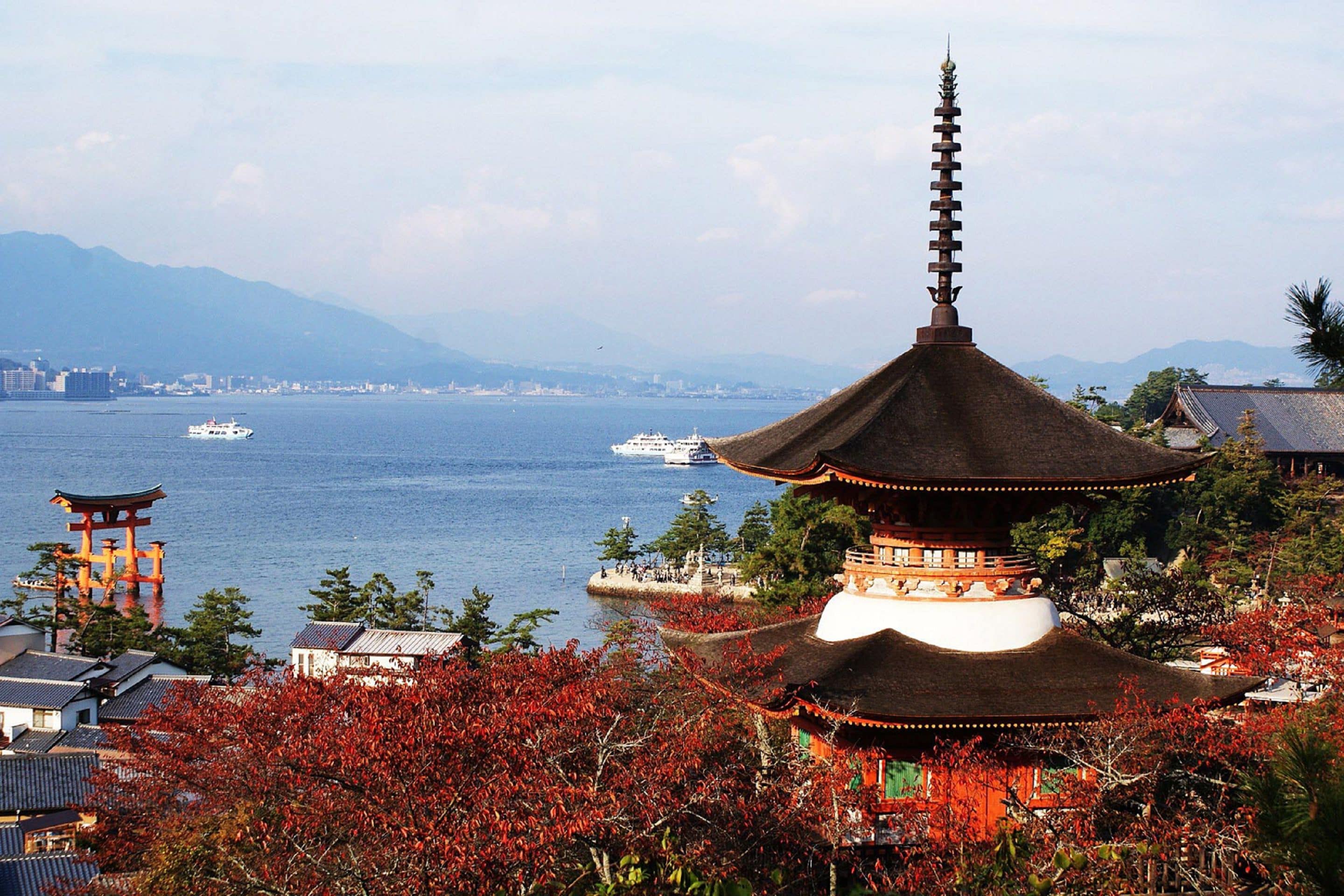 Una pagoda japonesa tradicional con techo de paja, con vistas a una masa de agua con barcos.