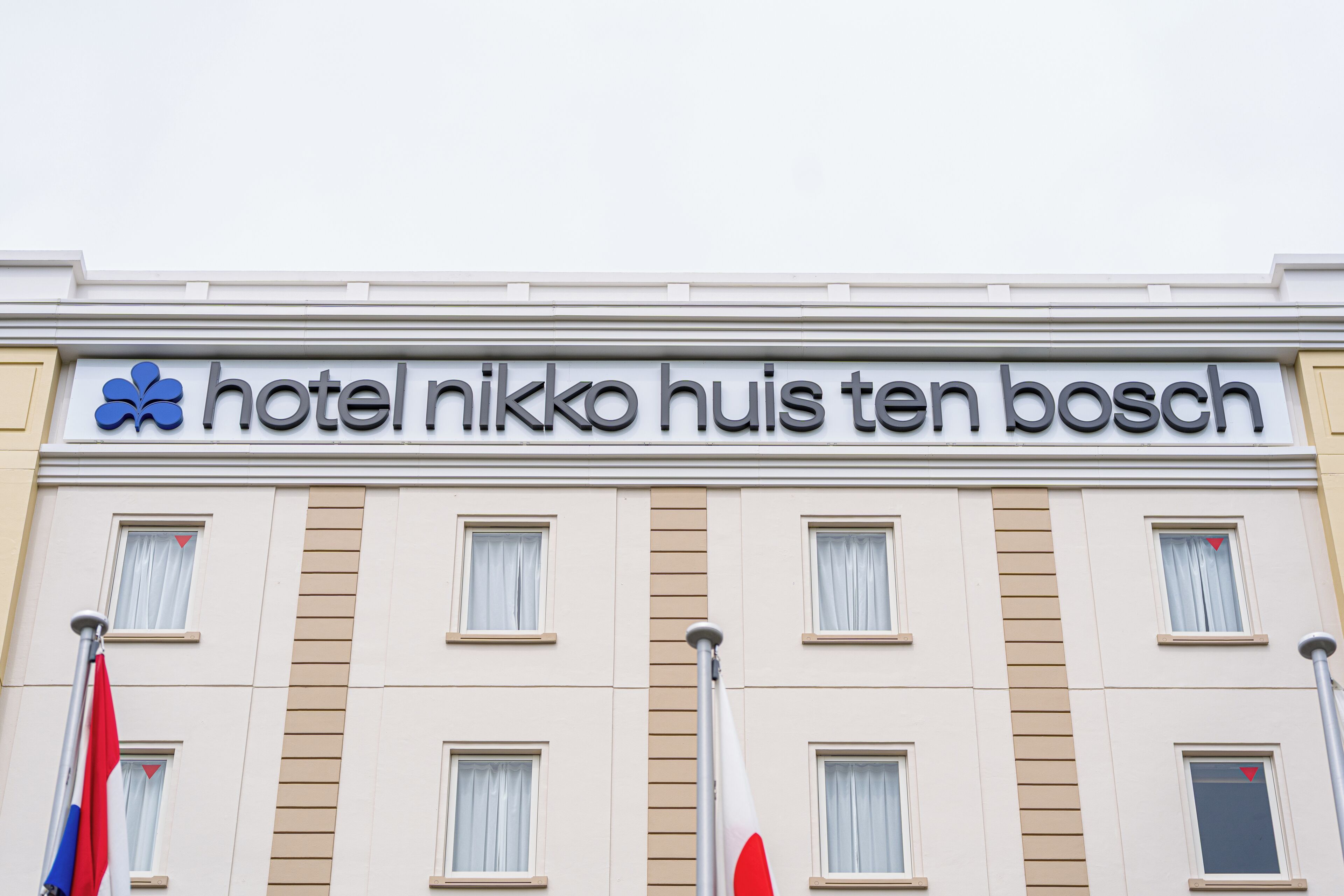 Une enseigne d’hôtel portant le nom « hôtel Nikko Huis Ten Bosch » et de nombreuses fenêtres avec des rideaux.