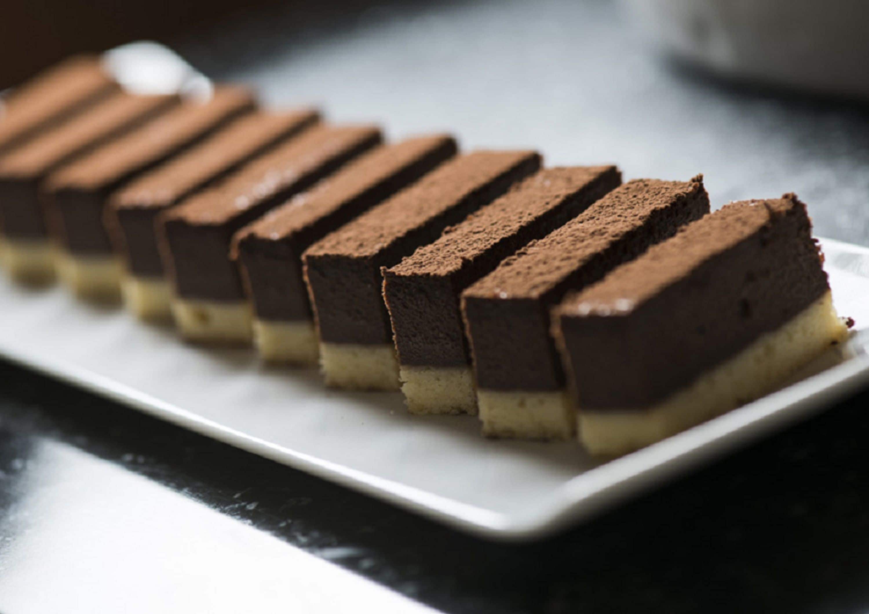 A white rectangular plate with several rectangular slices of layered dessert.