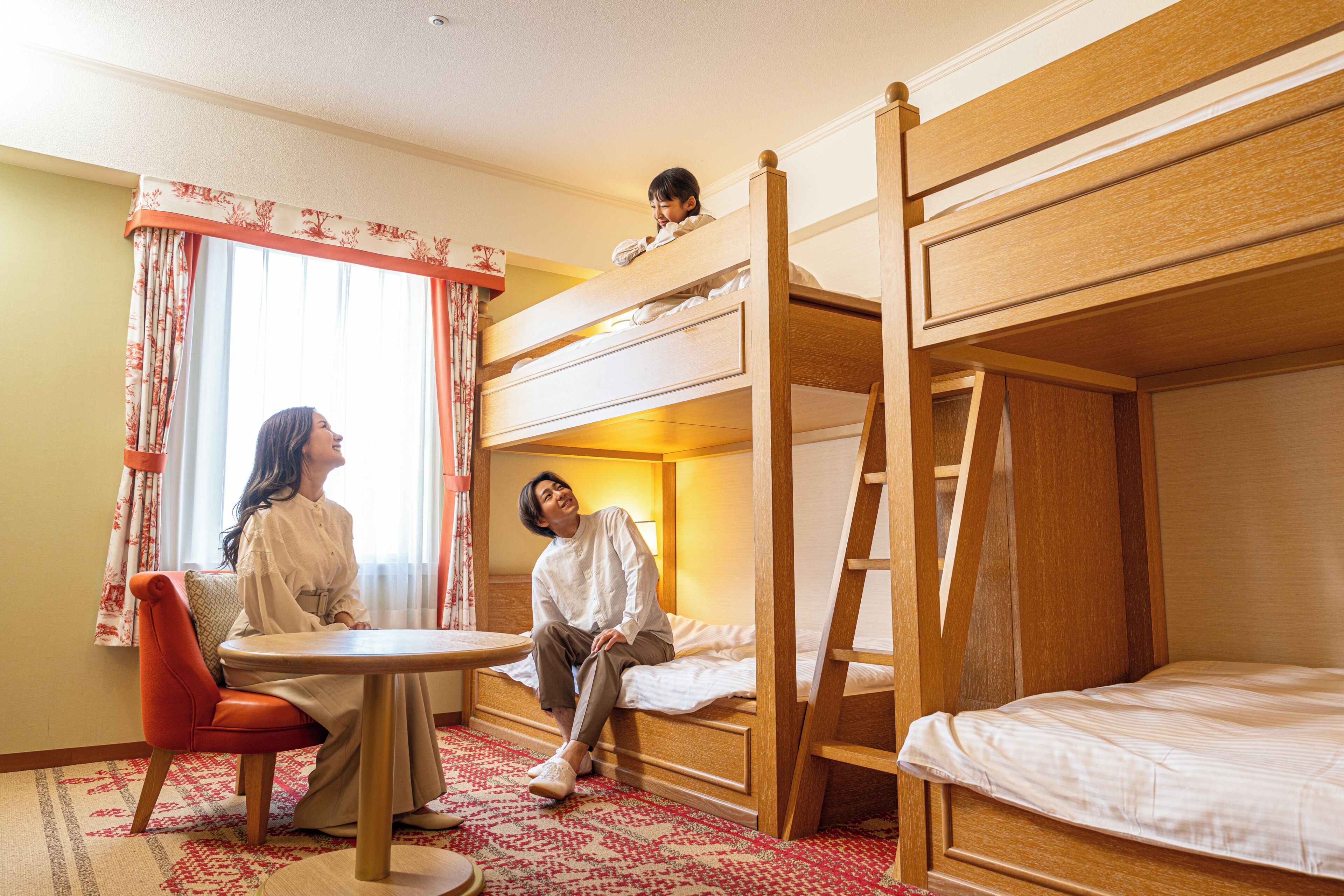 A hotel room with a bunk bed, a single bed, a round table, and a chair.