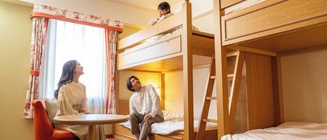 Hotellihuoneessa on kerrossänky, yksi erillinen sänky, pyöreä pöytä ja tuoli.