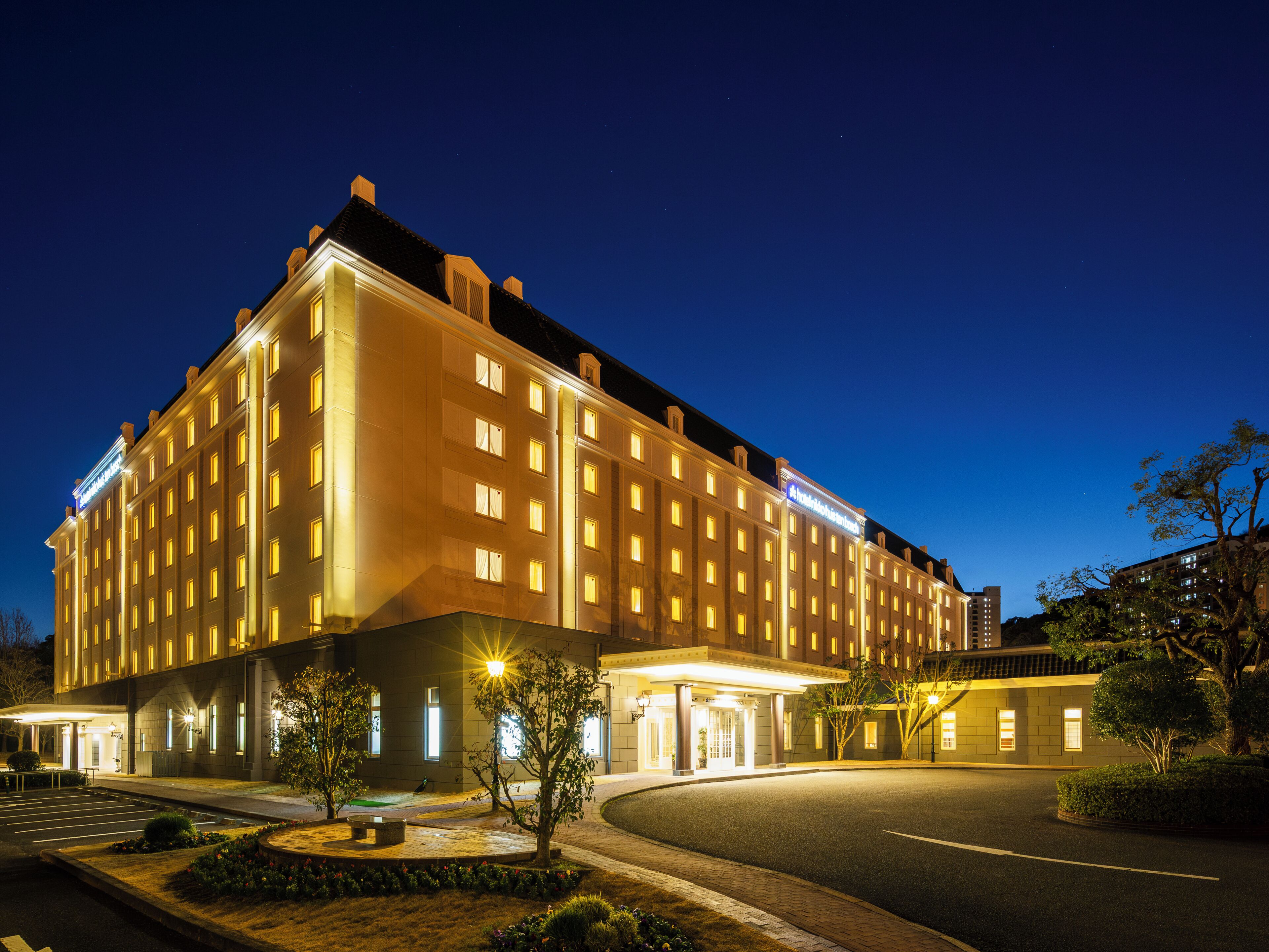 A large, multi-story hotel with a well-lit facade and a parking area in front.